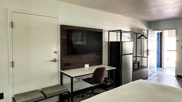 A compact hotel room with a single bed, a desk with a chair, a flat-screen TV, a small refrigerator, and a wardrobe.