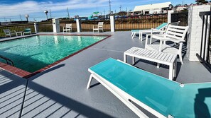 A rooftop pool with white lounge chairs and a small table.