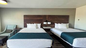 A hotel room with two beds, a nightstand, a lamp, a chair, and a small table.