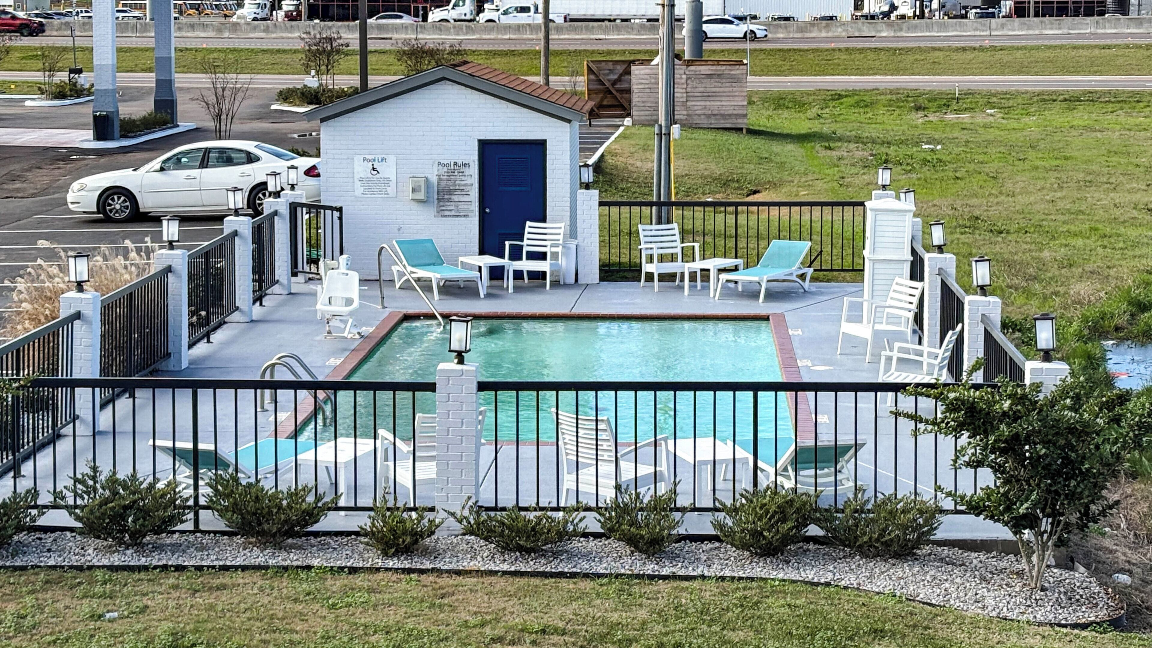 A pool area with a small building, lounge chairs, and a pool.