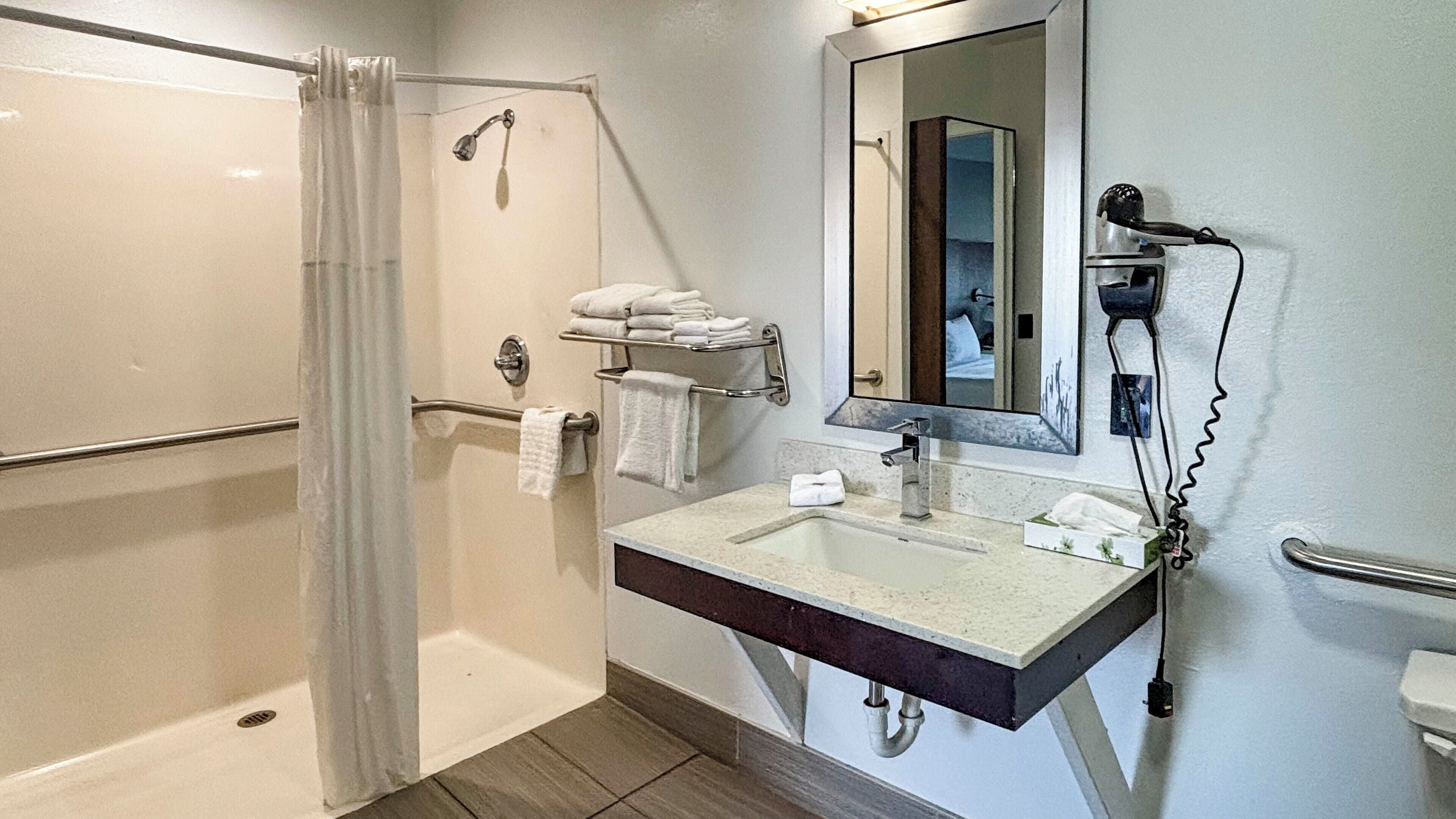 Un baño moderno con ducha, lavabo con espejo y un perchero para toallas.