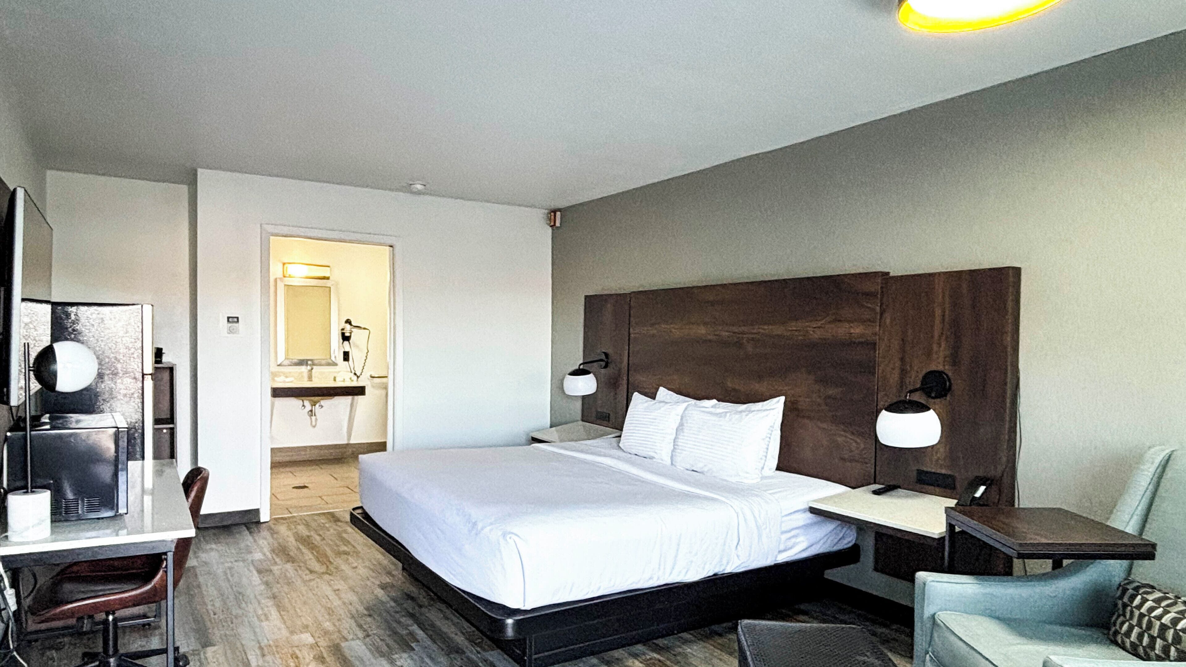 A hotel room with a large bed, a desk with a chair, a small table, and a sofa.