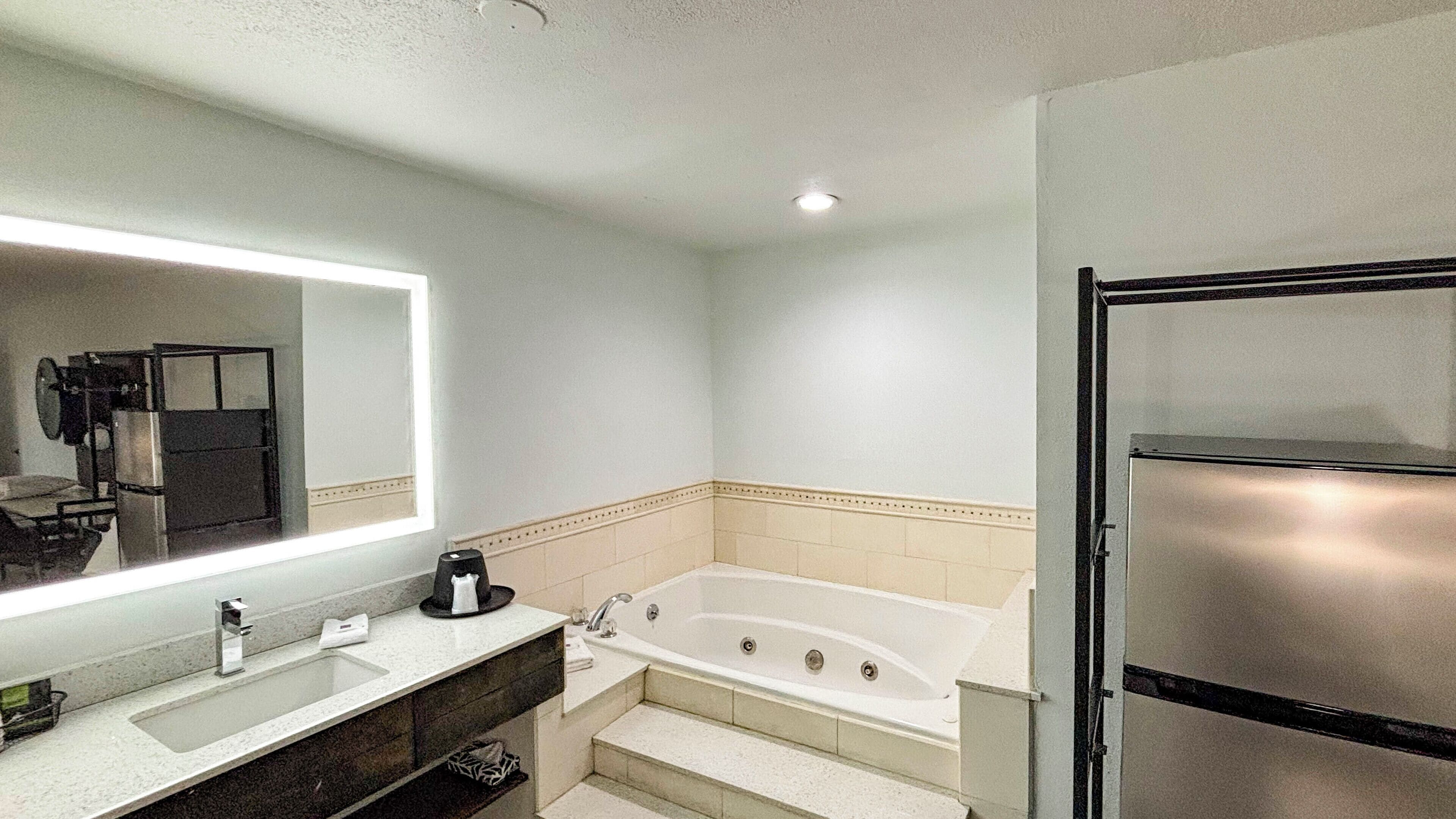 A bathroom with a large mirror, a bathtub, a sink, and a refrigerator.
