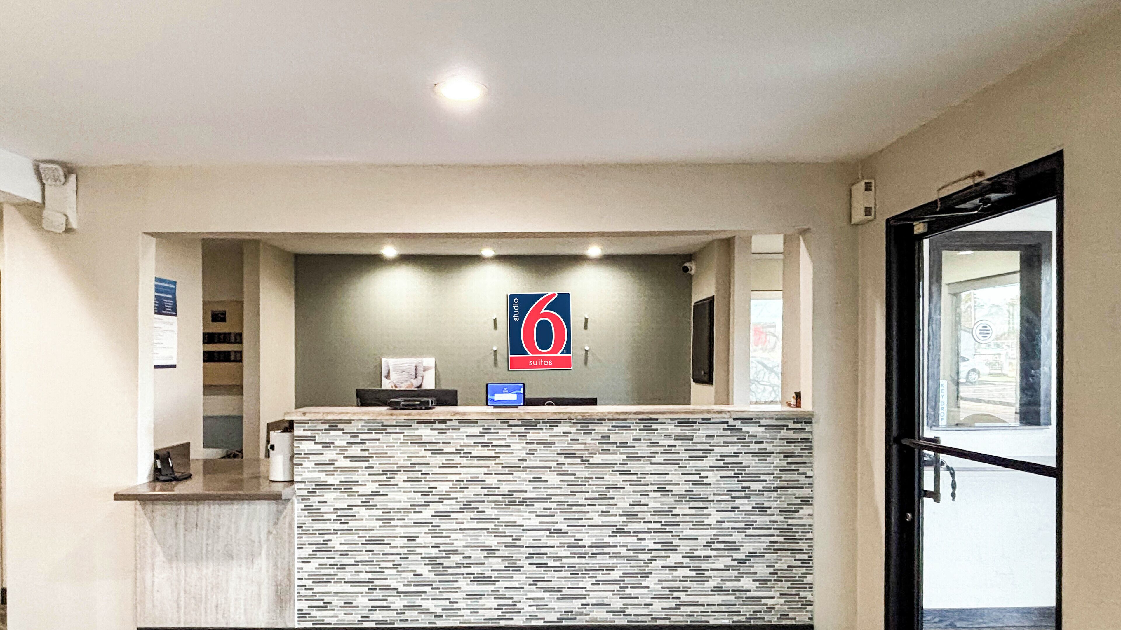 A hotel reception area with a modern design, a sign indicating '6 suites', and a reception desk with a computer and a small seating area.