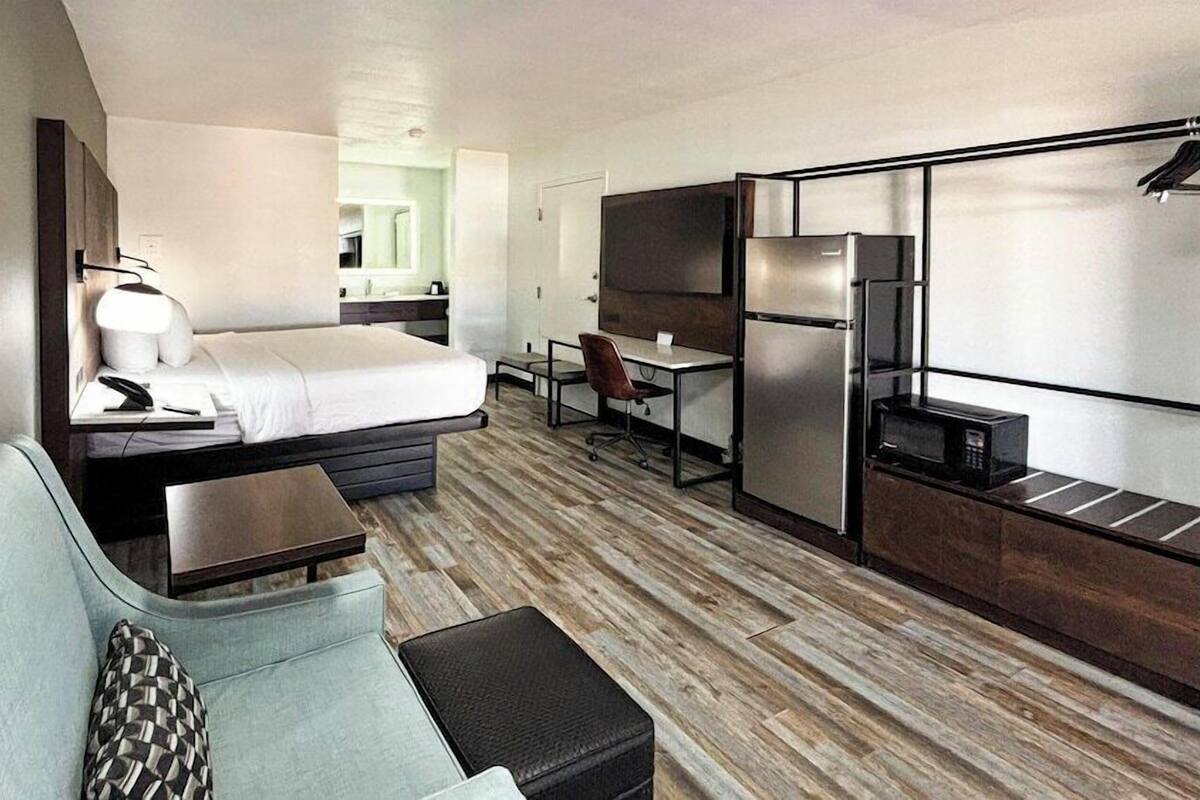 Ett kompakt hotellrum med en säng, en liten soffa, ett skrivbord, en stol och ett litet pentry.