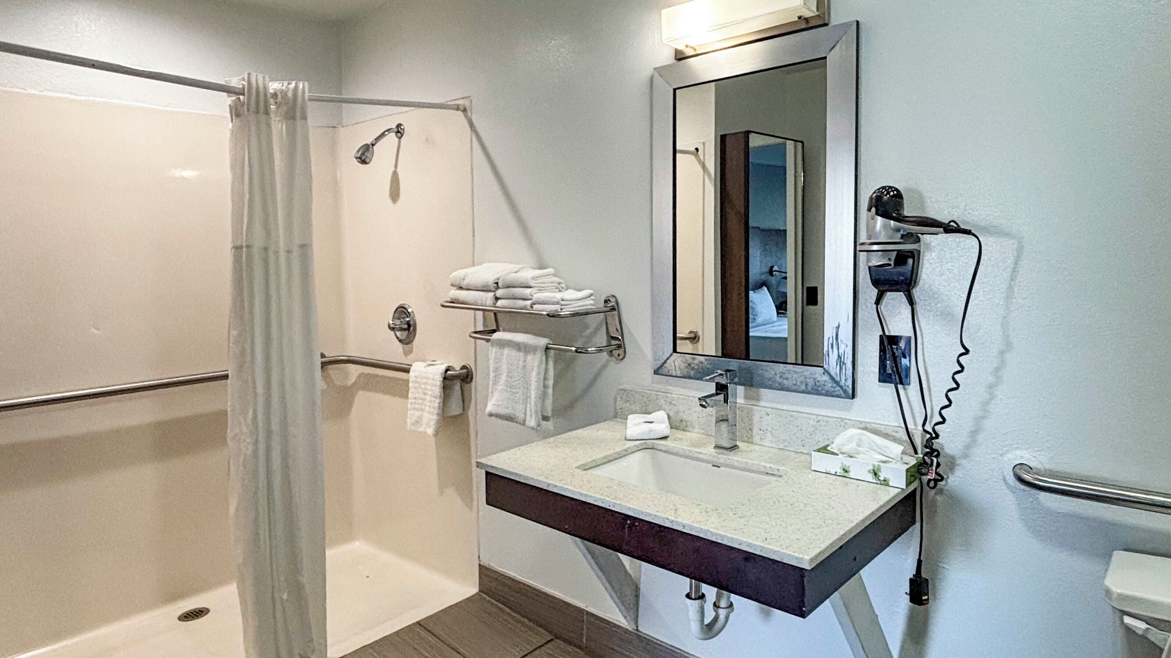 A bathroom with a shower, a sink, a mirror, and a towel rack.