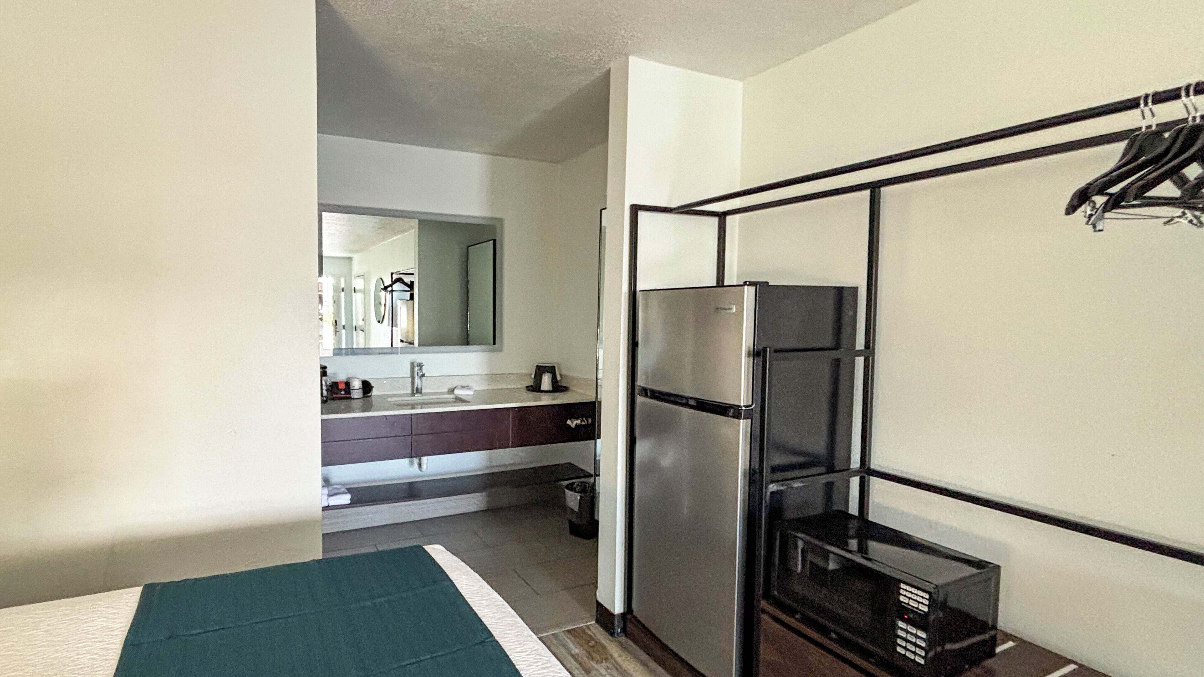 Habitación de hotel compacta con kitchenette, refrigerador, microondas y un pequeño cubo de basura.