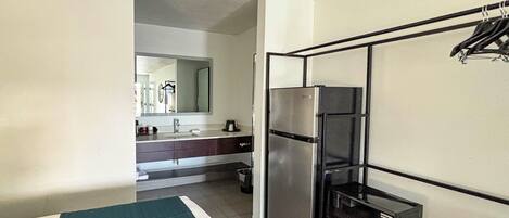 A compact hotel room with a kitchenette, a refrigerator, a microwave, and a small trash bin.