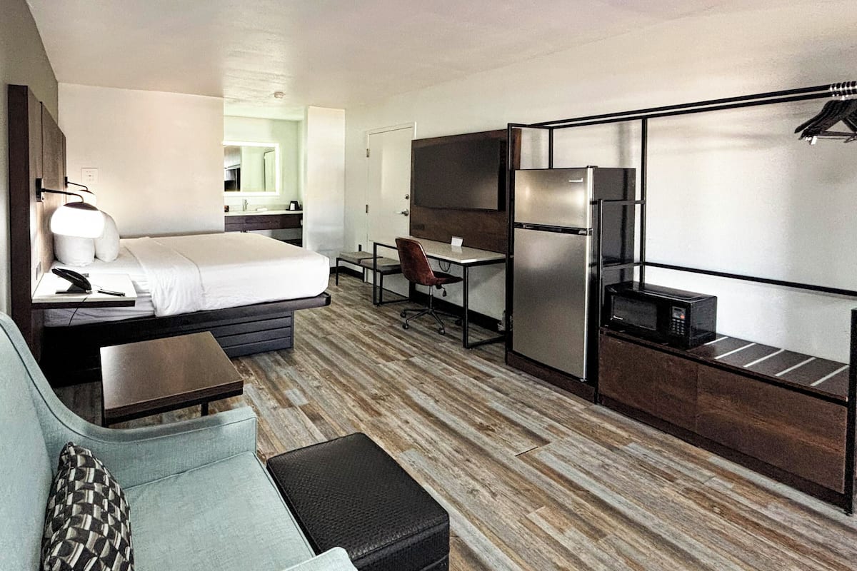 Ett kompakt hotellrum med en säng, en liten soffa, ett skrivbord och ett litet pentry.
