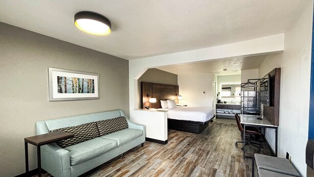 Habitaci ón de hotel con un sofá azul claro, una cama con cabecera de madera, un escritorio con una silla y un baño visible a través de un arco.