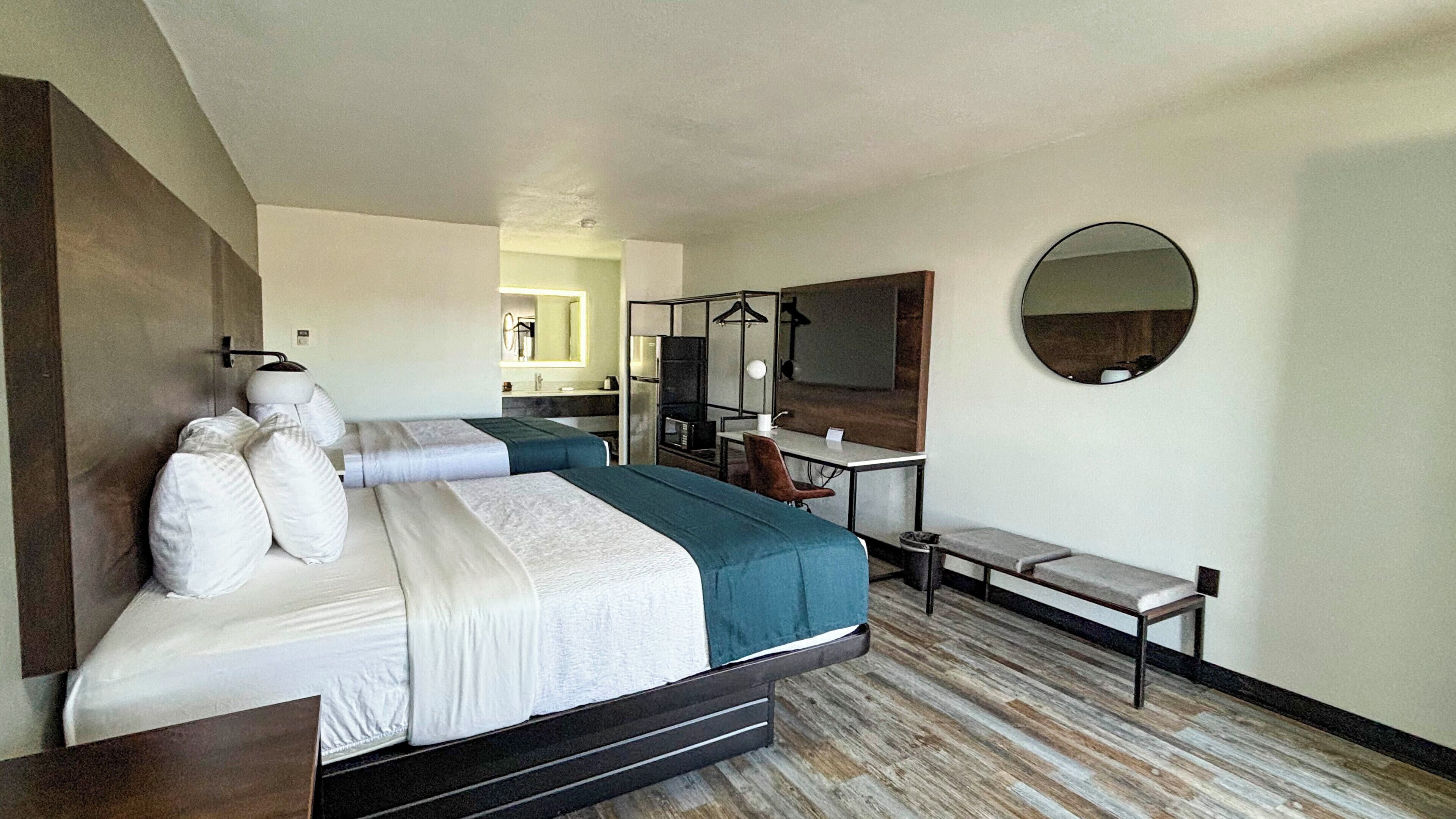 Habitación de hotel con cama, escritorio, silla, espejo y una pequeña zona de estar.