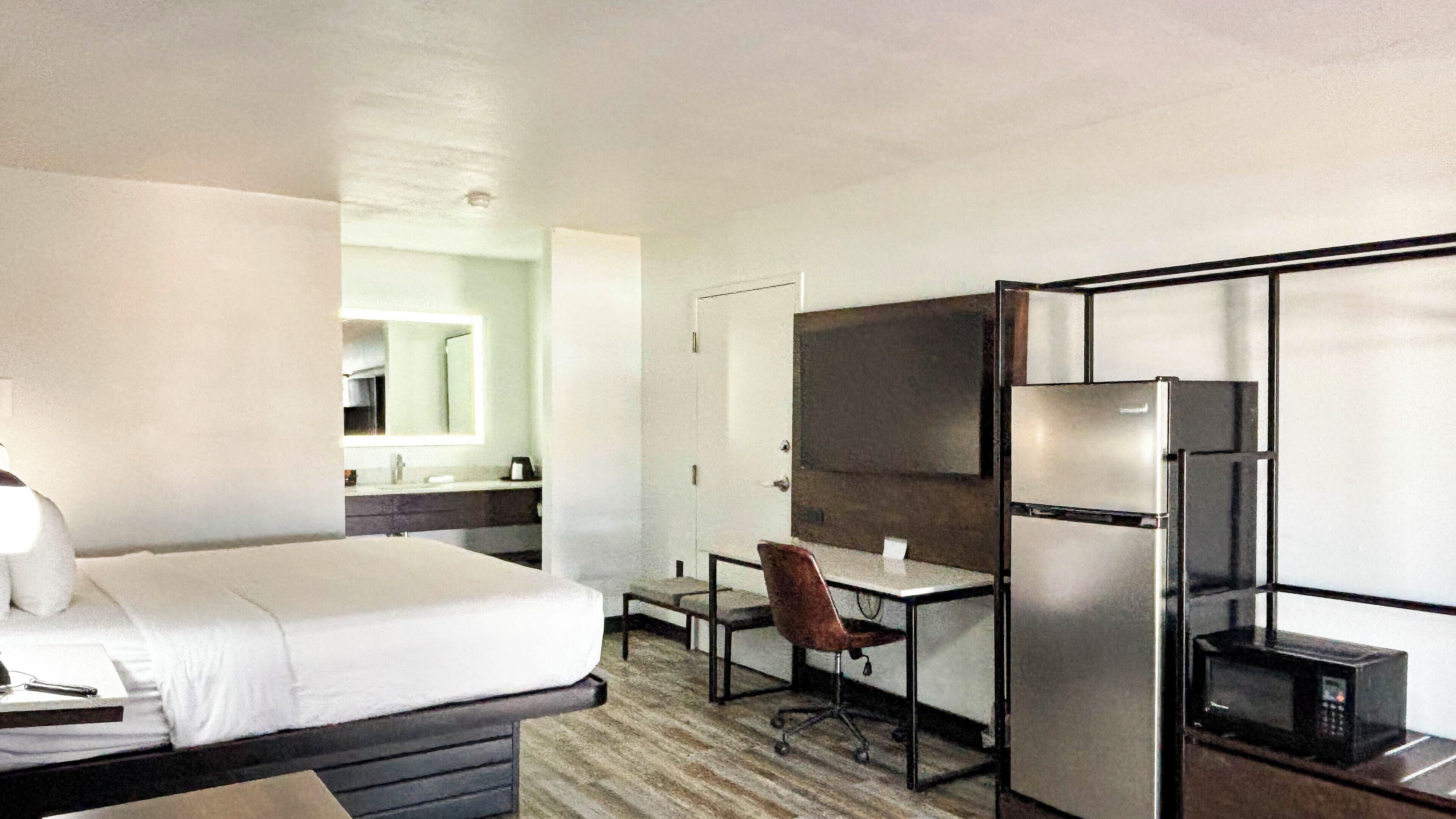 A hotel room with a bed, a desk, a chair, a refrigerator, and a microwave.