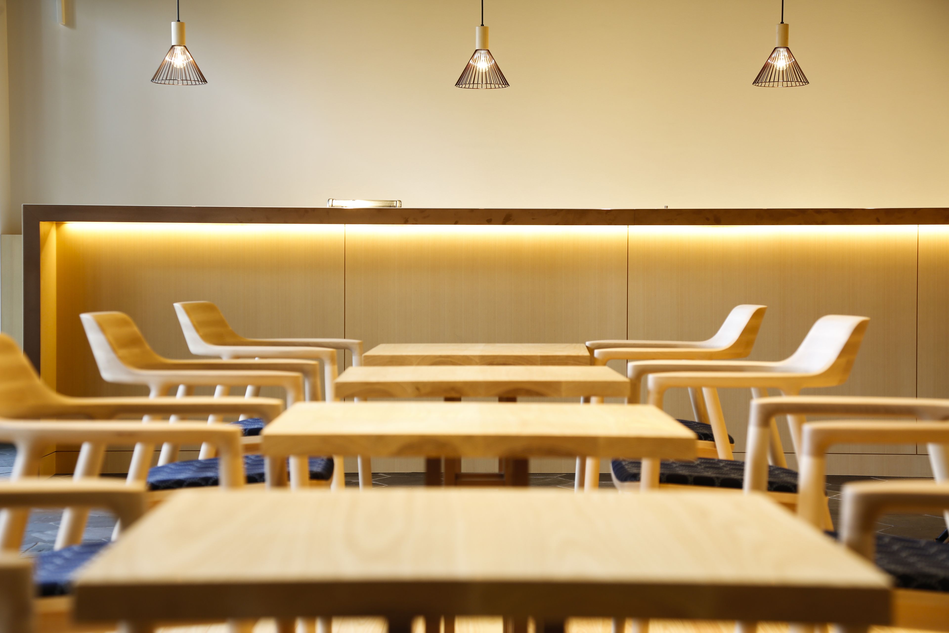 A modern waiting area with wooden tables and chairs, a reception desk, and pendant lighting.