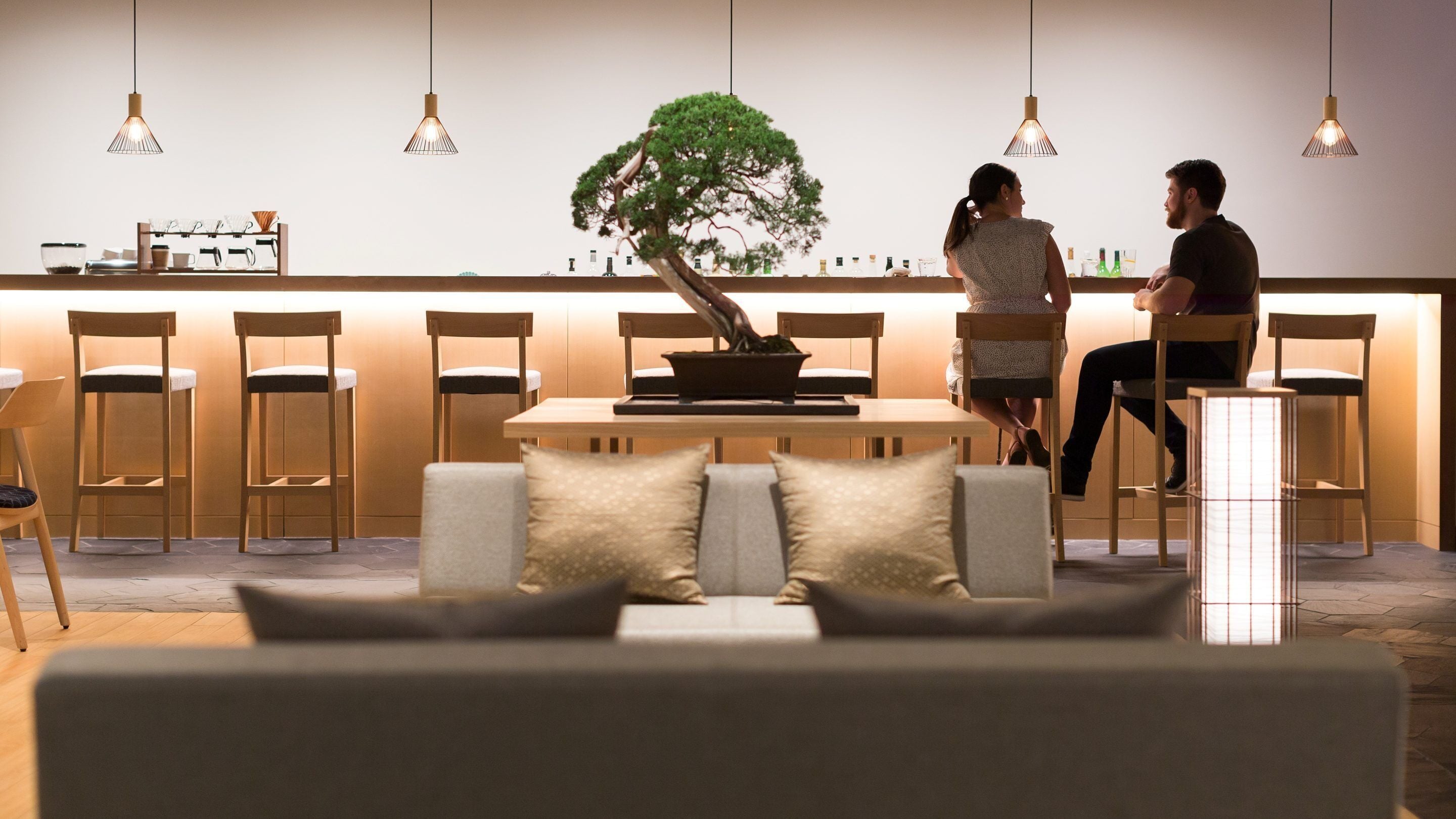 A modern dining area with a central table, chairs, a sofa, and a bonsai tree.