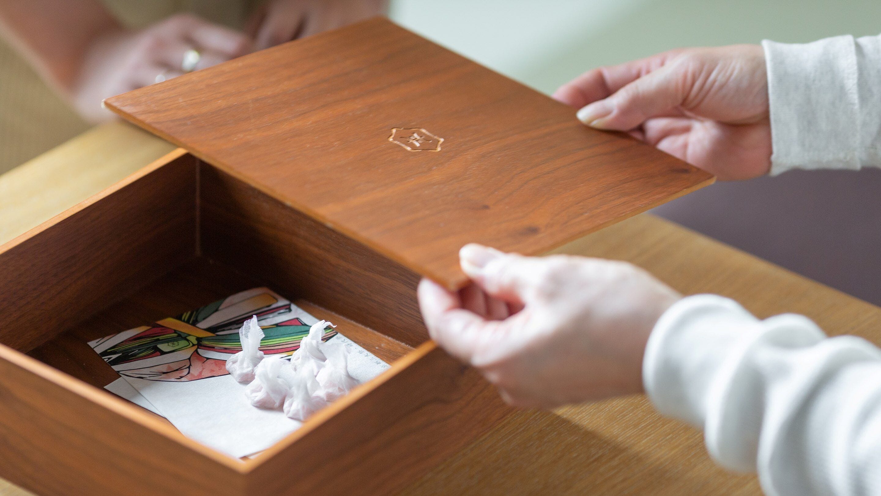 A wooden box with a lid being opened, revealing colorful cards and tissues inside.