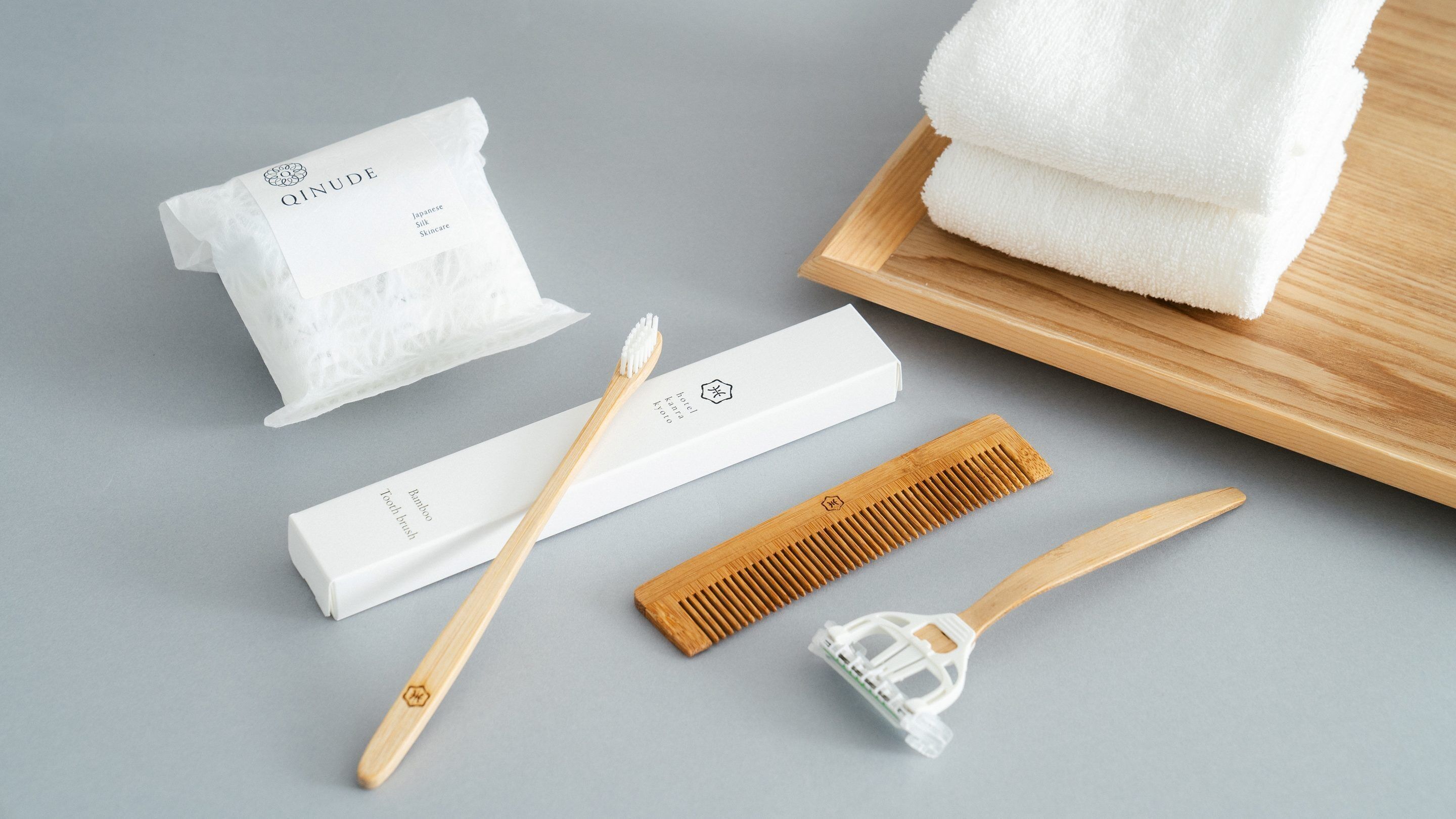 Un baño con una toalla blanca, un cepillo de dientes de bambú, un peine de madera y un rastrillo blanco sobre una superficie gris.