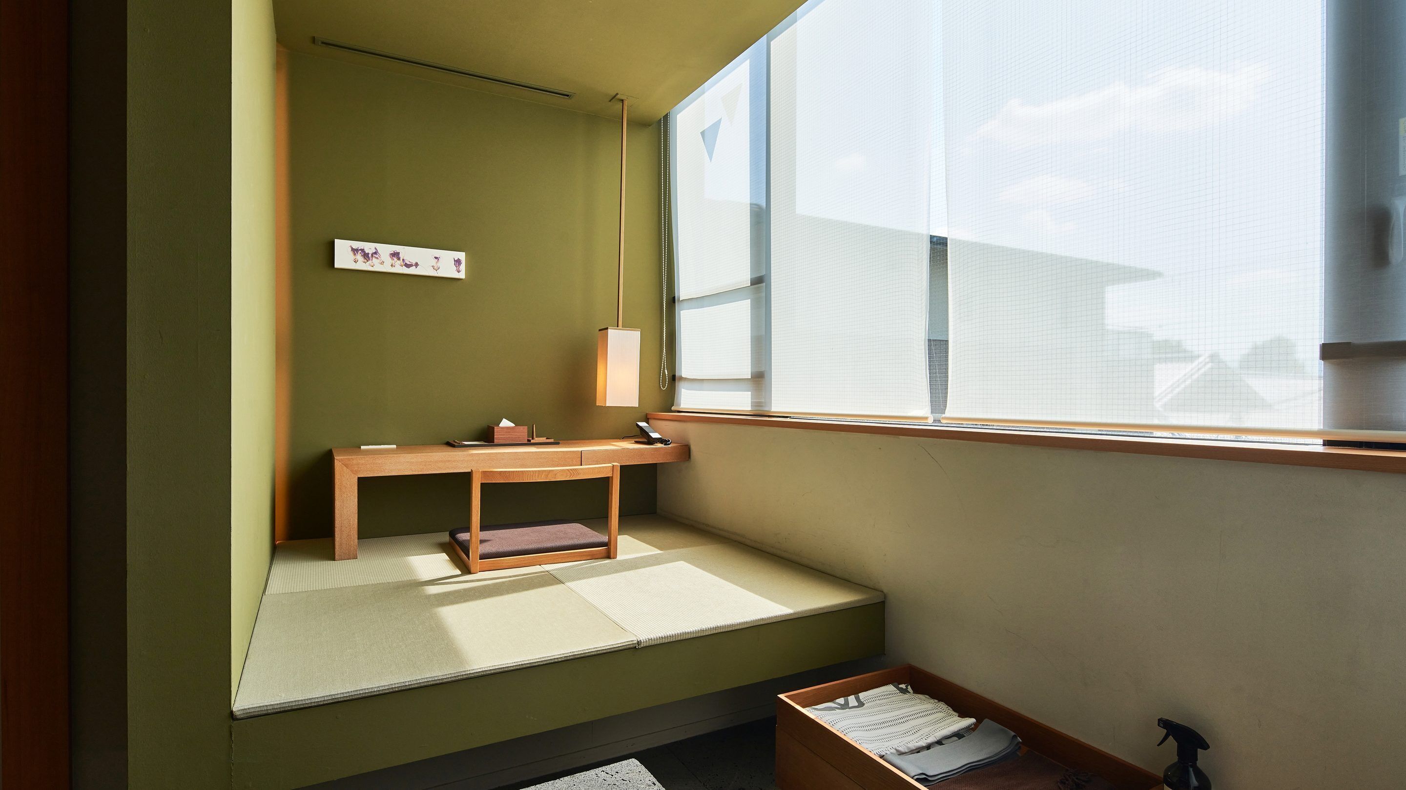 A room with a tatami mat floor, a wooden desk with a lamp, and a window with a view.