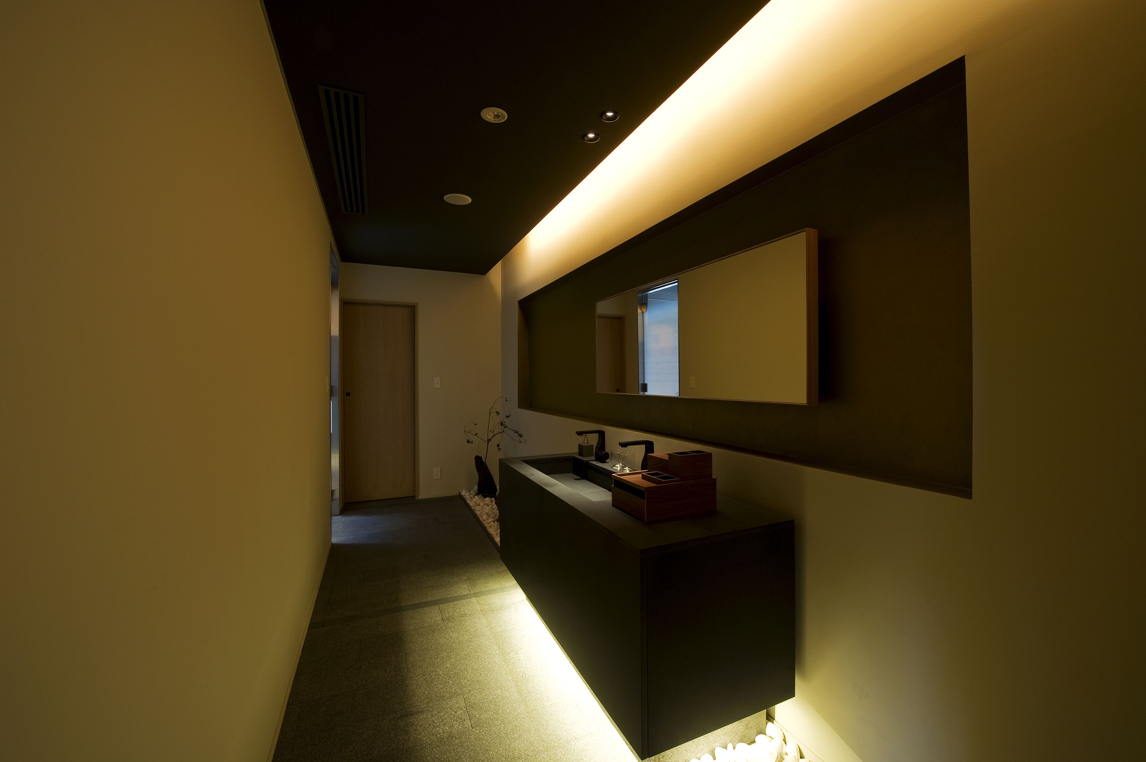 A modern bathroom with a dark sink, a mirror, and a light fixture.