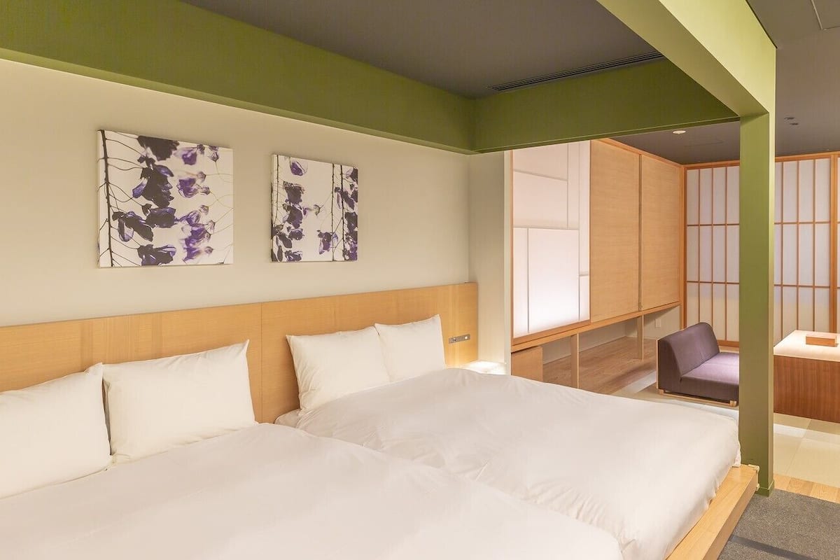 A hotel room with two beds, a seating area, and traditional Japanese sliding doors.