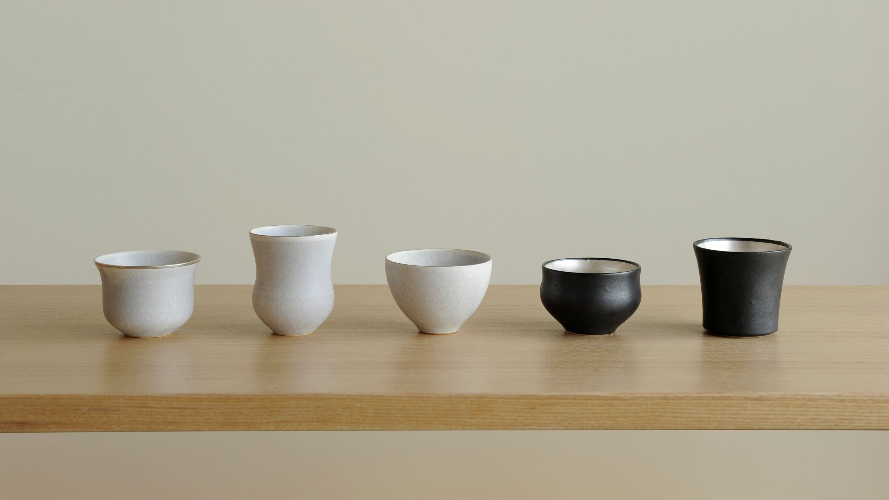 Cinco tazas de cerámica sobre una repisa de madera.