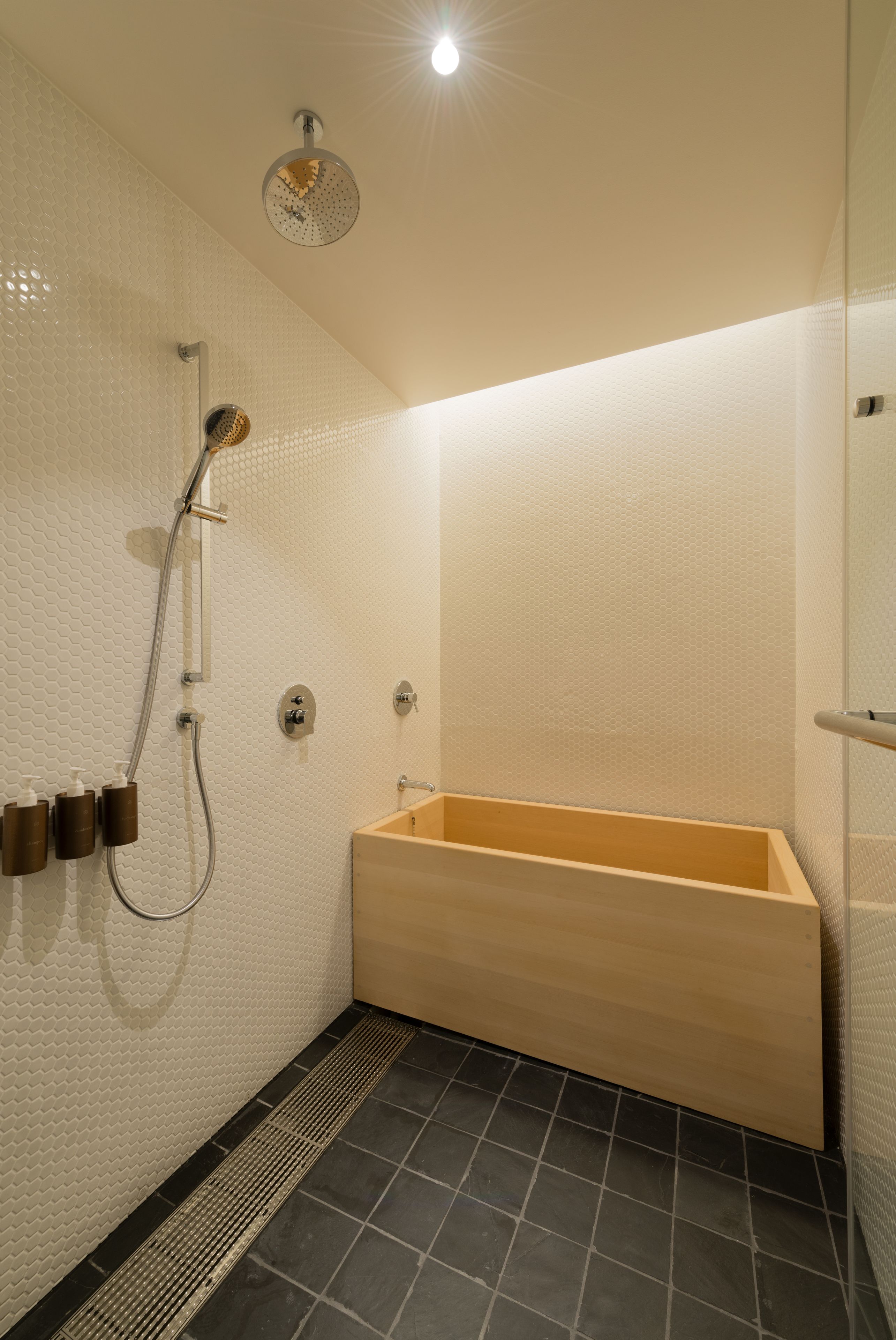 A modern bathroom with a wooden bathtub, a handheld showerhead, and a wall-mounted faucet.