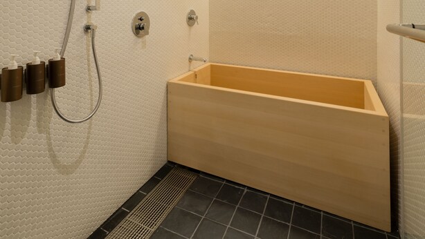 A modern bathroom with a wooden bathtub, a handheld showerhead, and a wall-mounted faucet. - Hotel Kanra Kyoto (Kyoto)