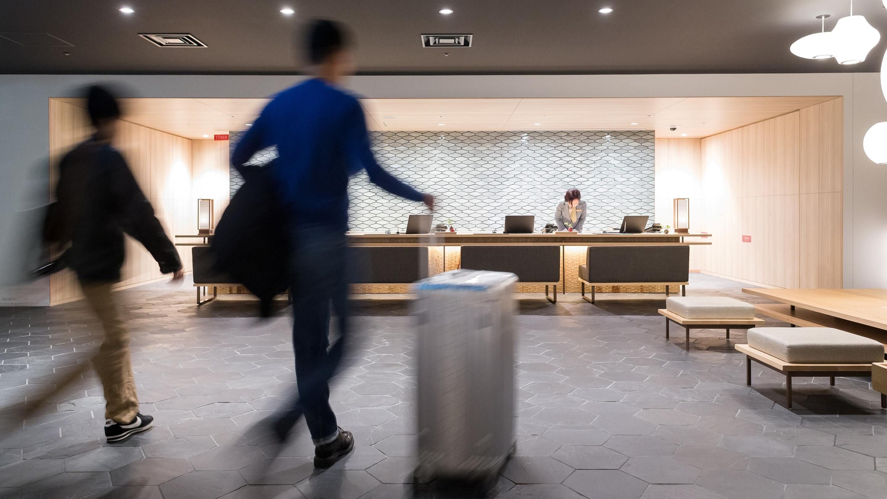 Un hall d’hôtel moderne avec un comptoir d’accueil, des espaces de détente et un mur décoré de motifs.