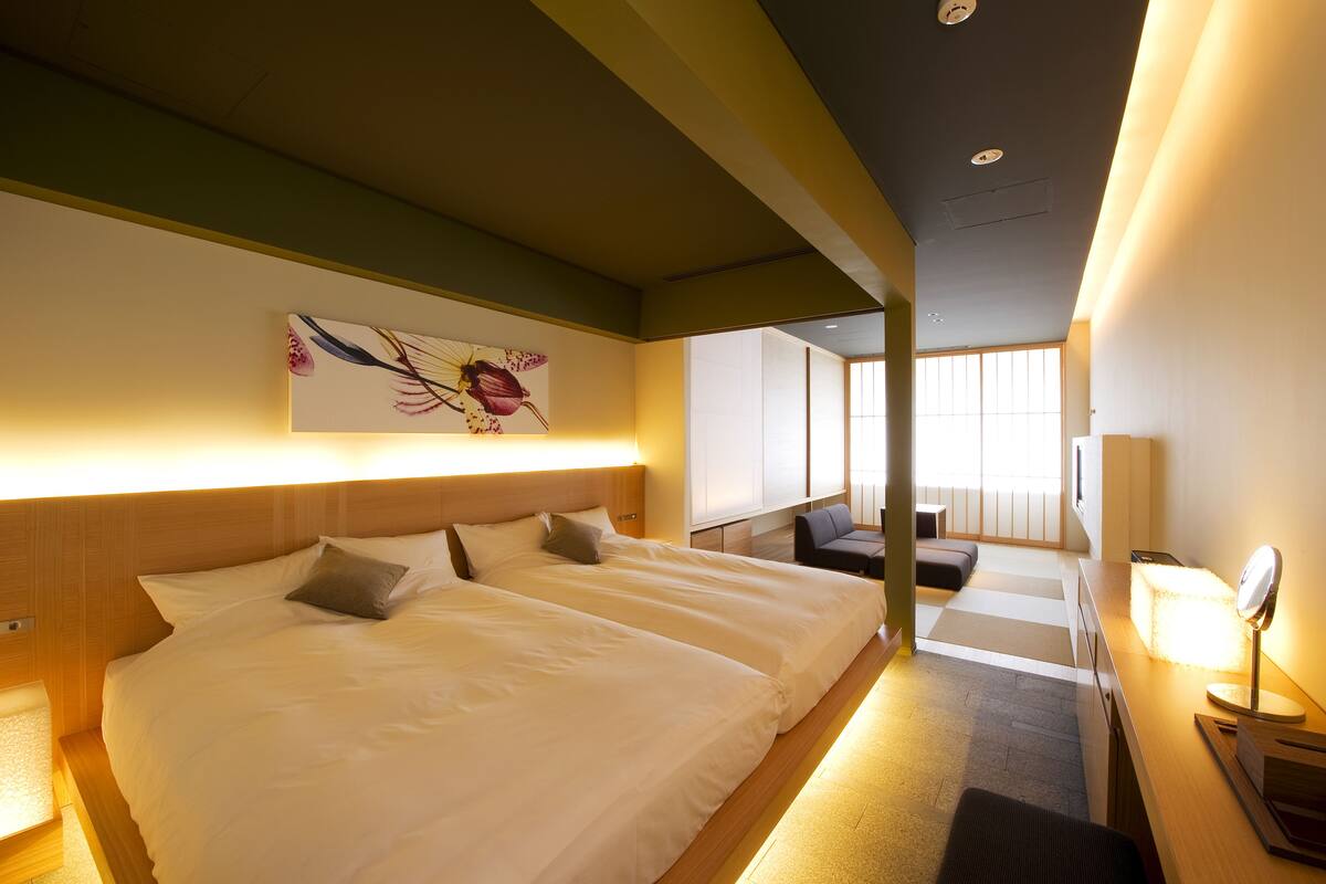 Una habitación de hotel con dos camas, un escritorio con lámpara, una silla y un ventanal grande.