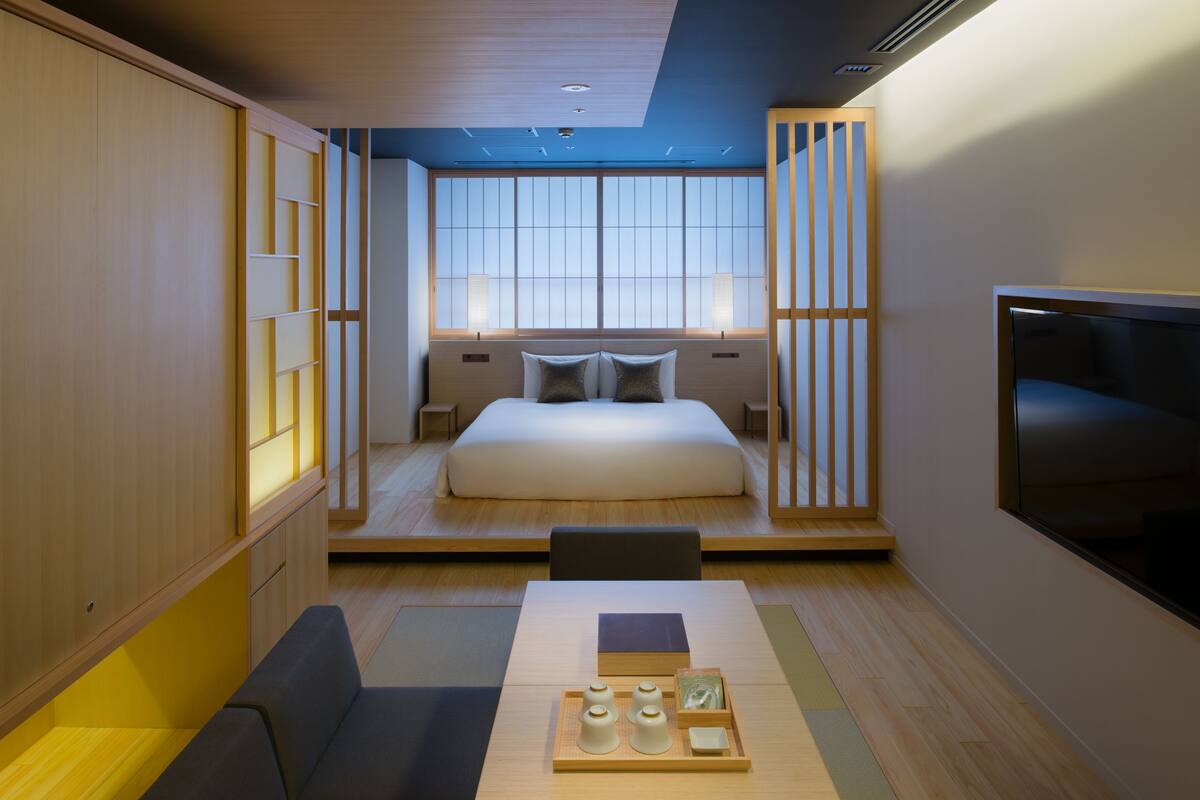 Una habitación de hotel moderna con una cama grande, un televisor, un sofá y una bandeja con objetos sobre la mesa.