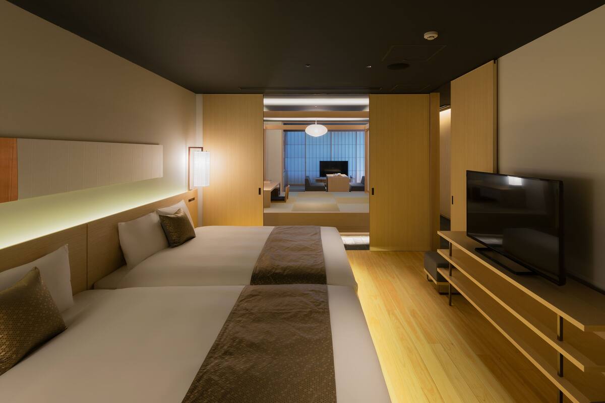 Una habitación de hotel moderna con una cama grande, televisión y un área de descanso con vistas a la ciudad.