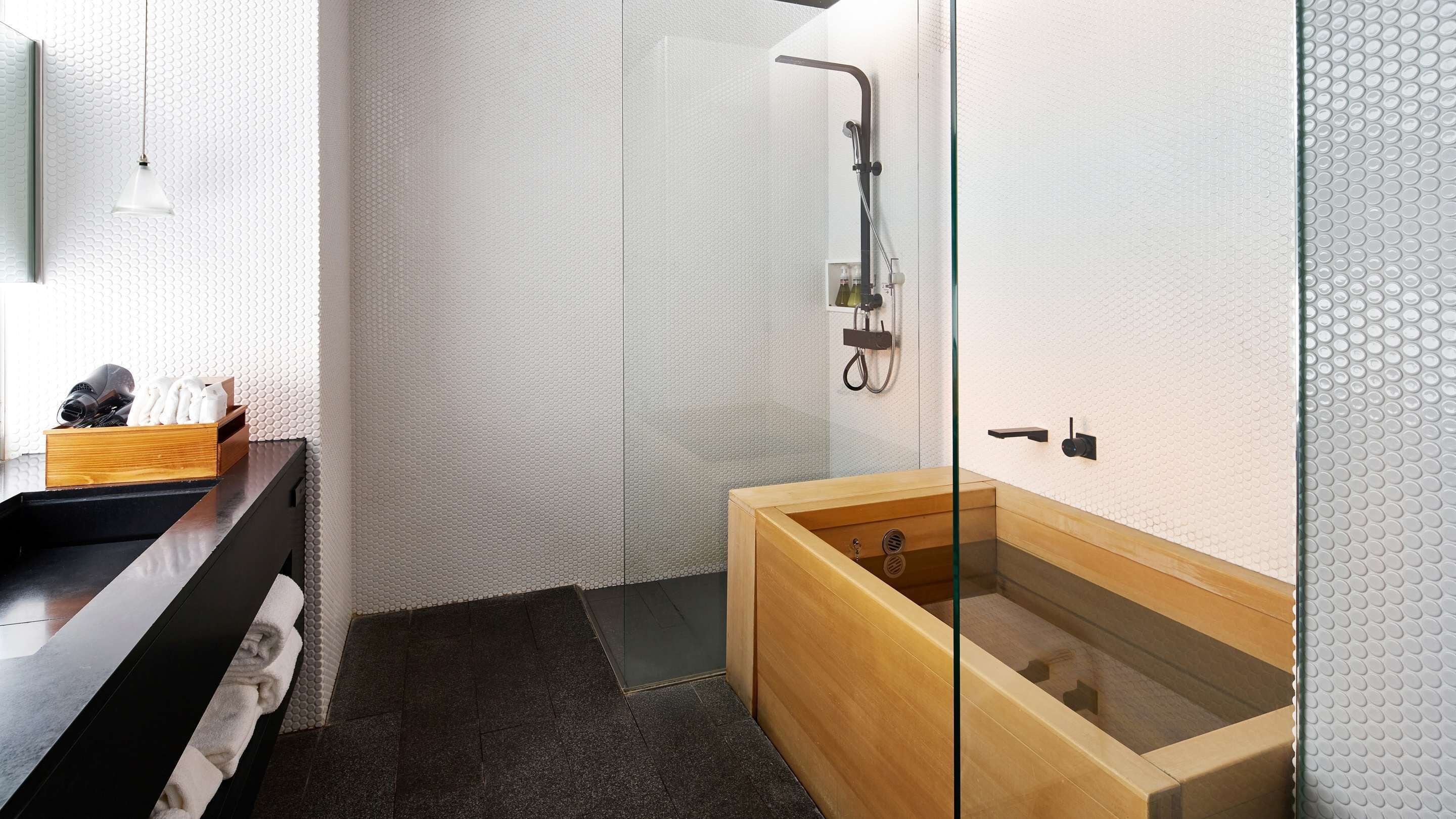 A modern bathroom with a wooden bathtub, a glass shower enclosure, and a black vanity with a towel.