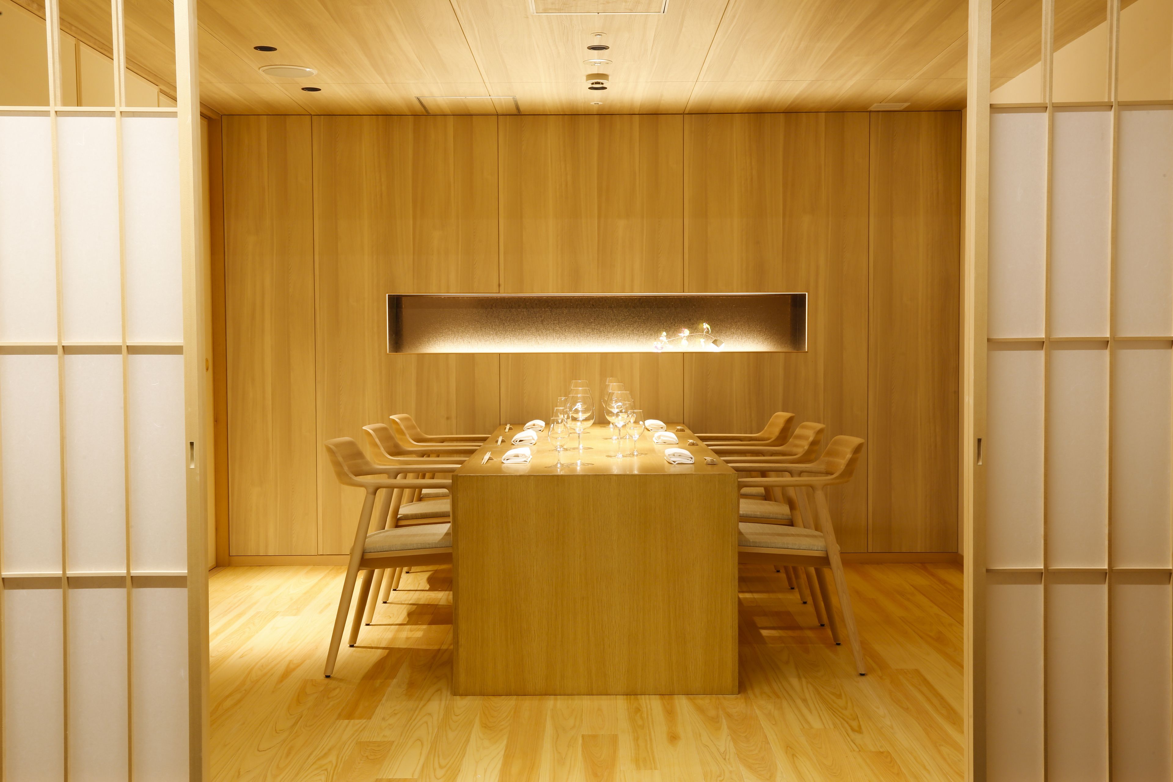 A wooden interior with a central table set for dining, surrounded by chairs.