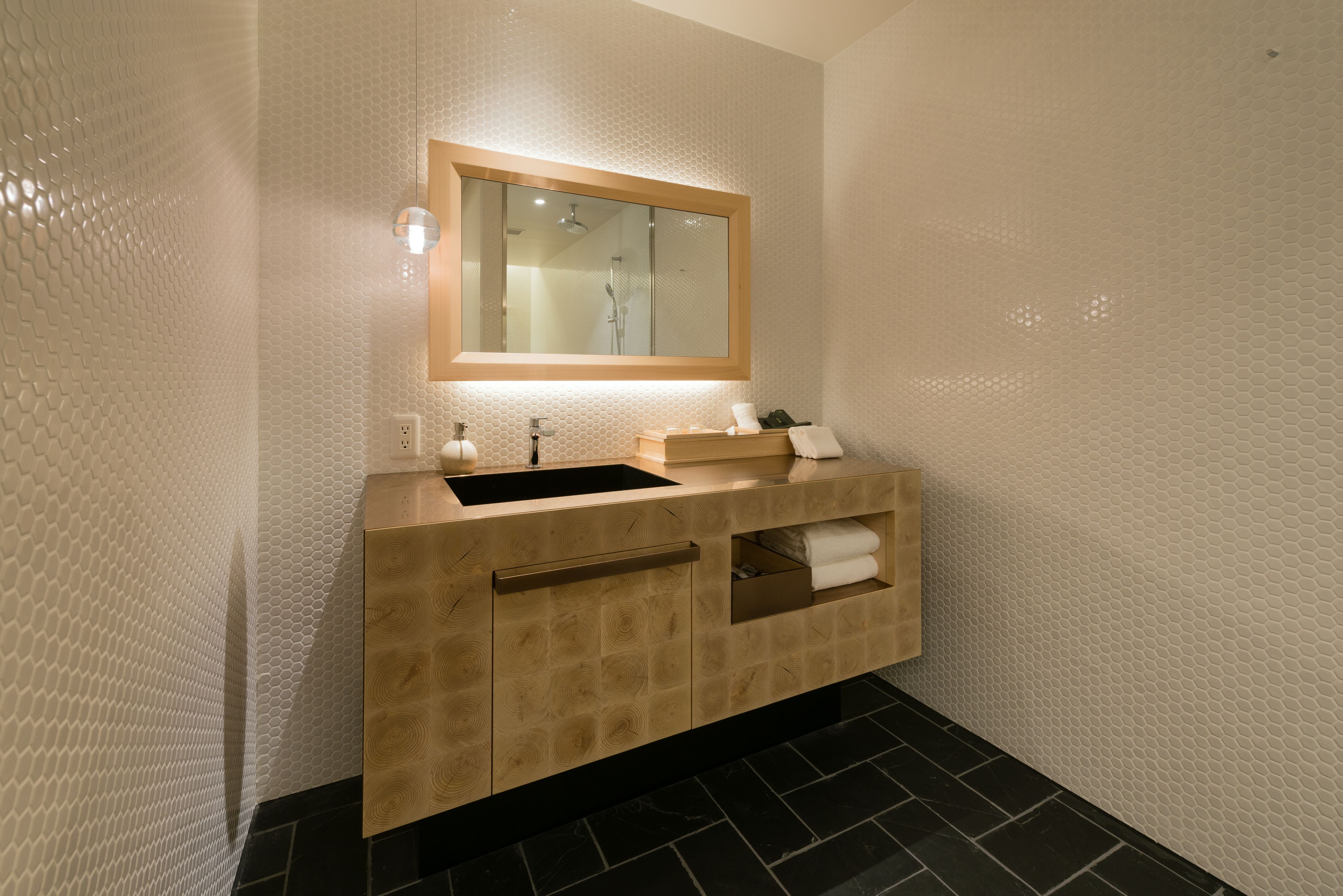 A modern bathroom with a wooden vanity, a mirror, and a black tiled floor.