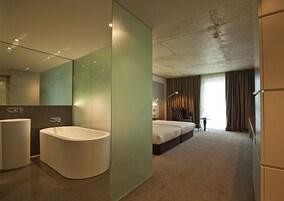 Una habitación de hotel moderna con una bañera grande, un dormitorio independiente con una cama, una silla y un escritorio.