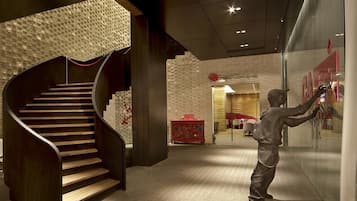Un interior moderno con una escalera espiral, una pared de cristal con un cartel rojo y una estatua de una persona.
