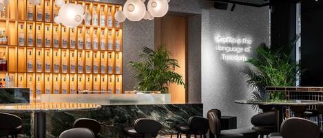 Zona de bar moderna con encimera de mármol, diversas opciones de asientos y una pared con botellas ordenadas.