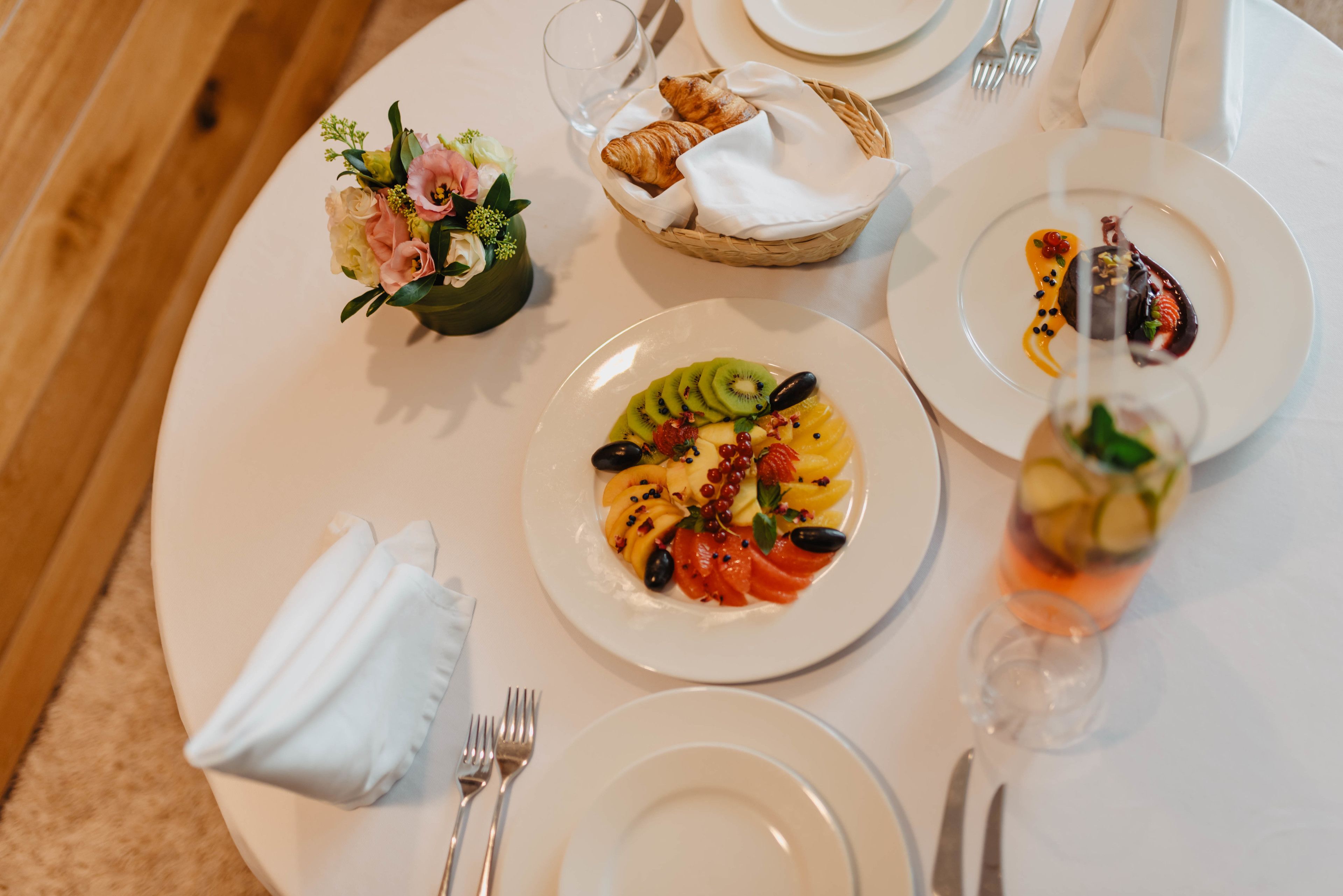 Une table à manger avec des assiettes remplies de nourriture, un panier de croissants et un petit bouquet de fleurs.