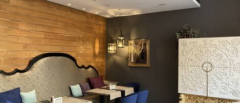 A modern restaurant with wooden panel walls, blue chairs, and a decorative cabinet.