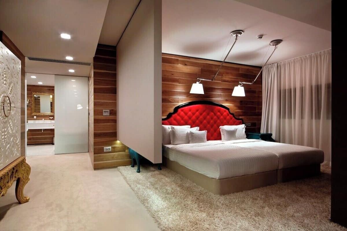 A modern hotel room with a large bed, a wooden headboard, and a separate bathroom visible through an open door.