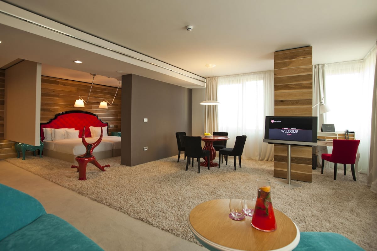 A modern hotel room with a bed, a TV, a dining area, and a living room.