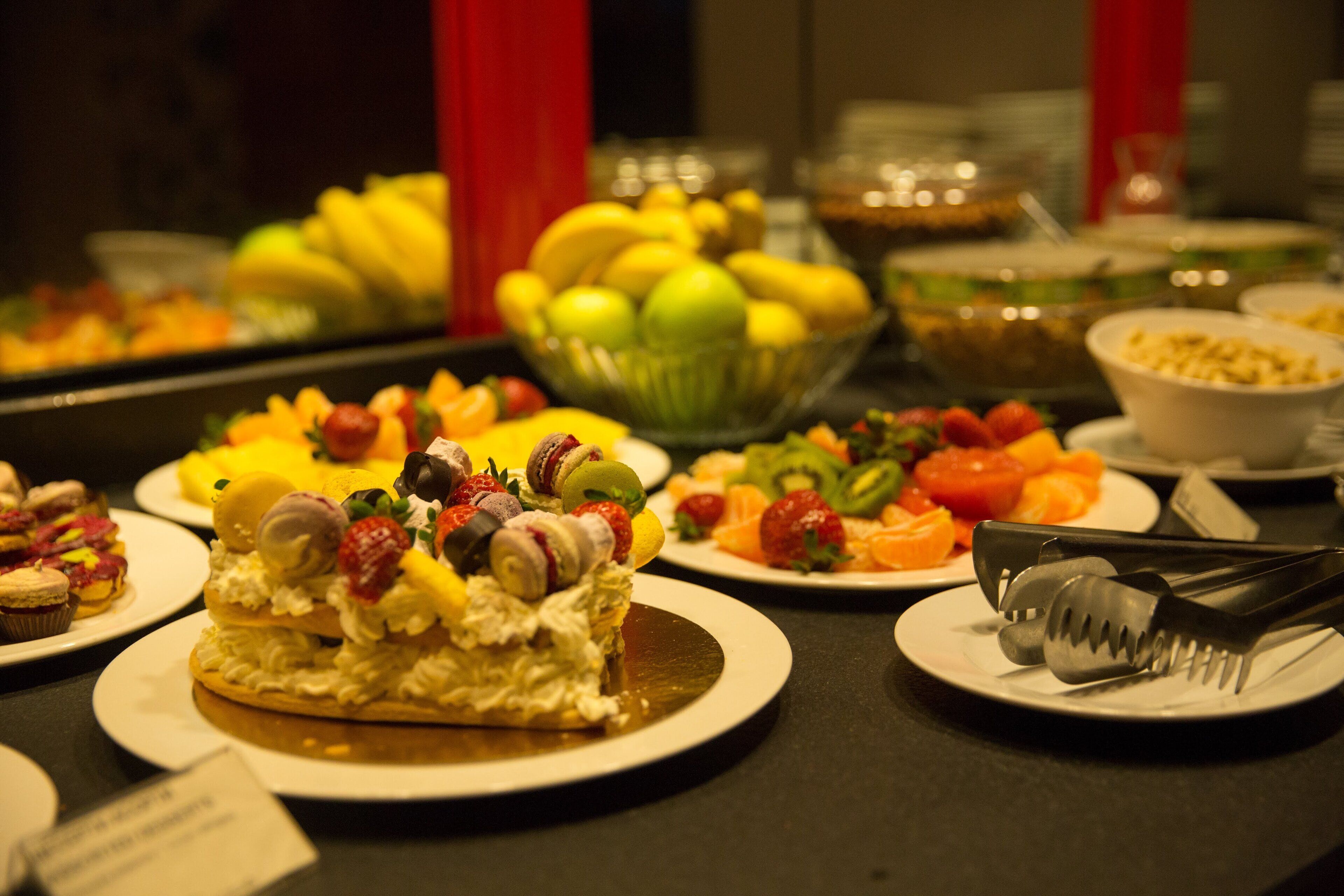 A buffet with various dishes including fruits, pastries, and a cake.