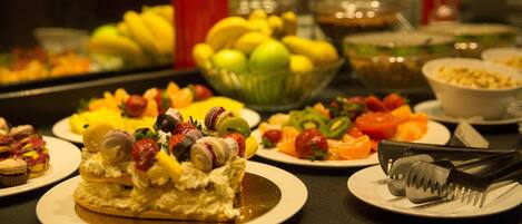 Un bufé con diversos platos, entre ellos frutas, pasteles y un pastel.