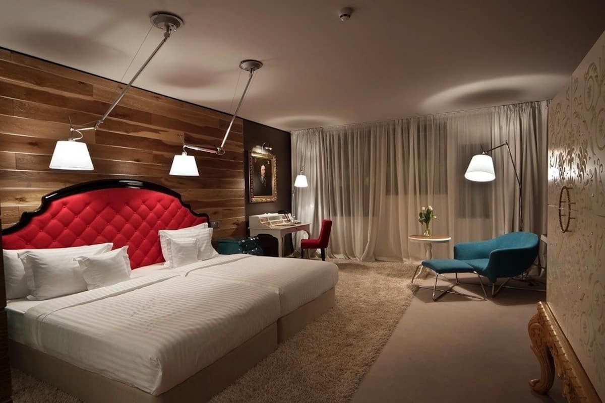 A hotel room with a large bed, a desk, a chair, and a small table with a vase of flowers.