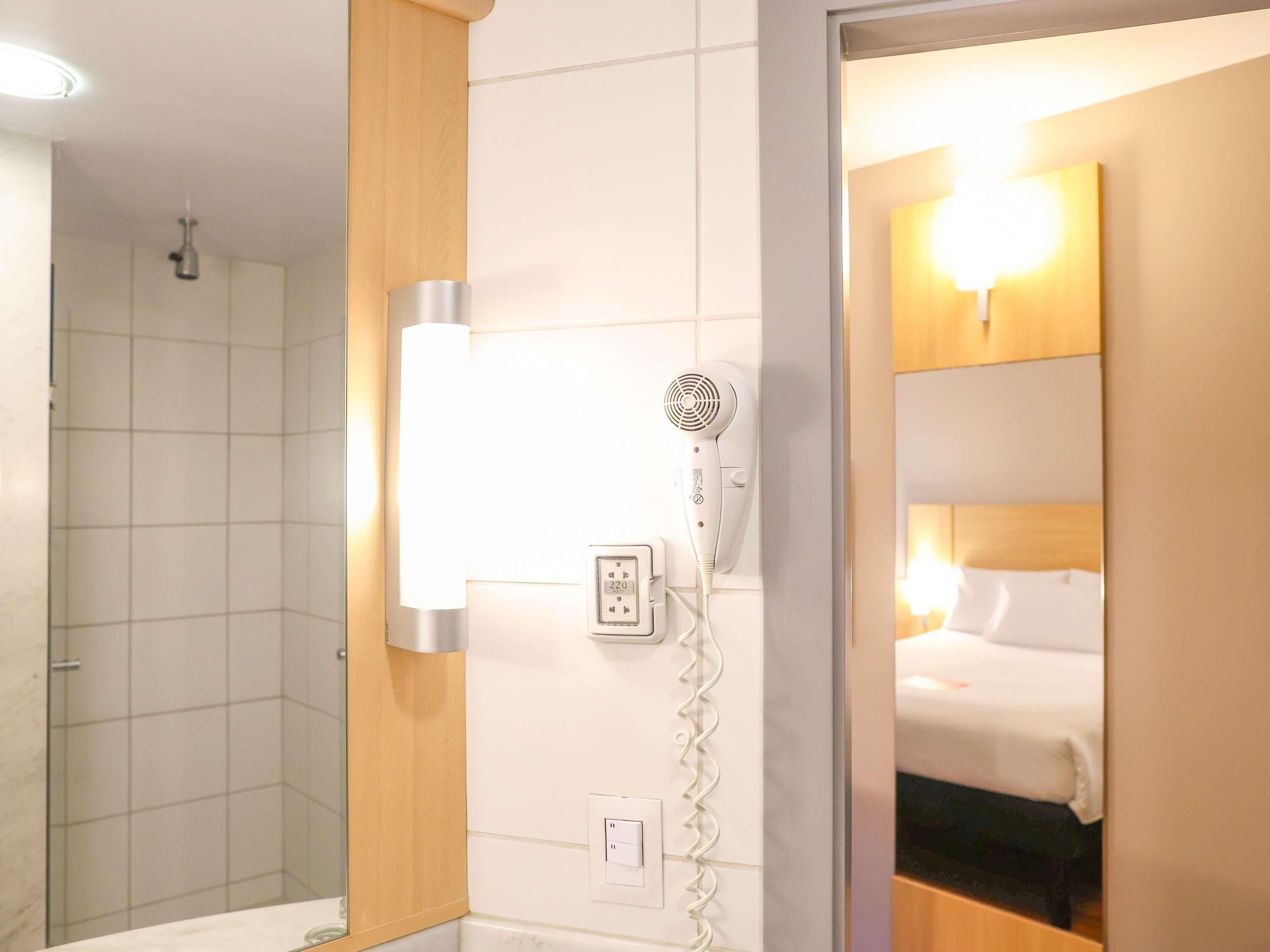 Ein Hotelzimmer mit Dusche, Föhn und einem Bett.