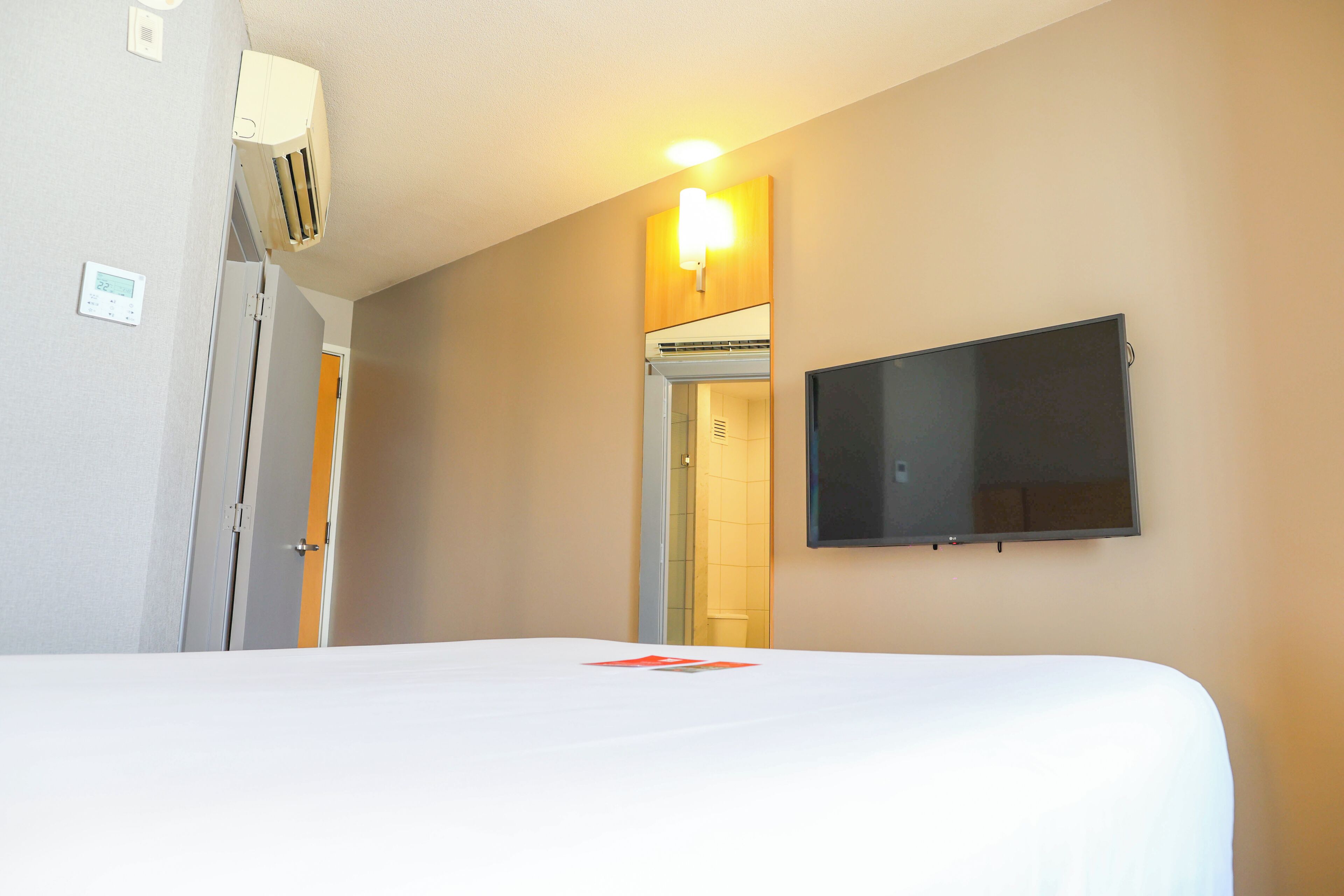 Una camera d'albergo con un letto, una TV a schermo piatto montata a parete, un condizionatore d'aria e un ingresso che dà su un bagno.