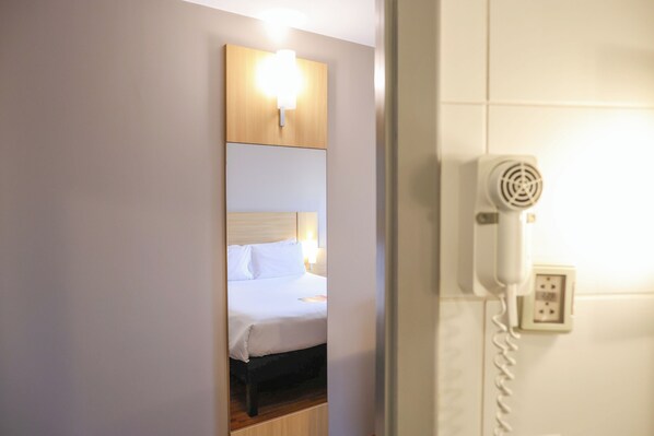 Una habitación de hotel con una cama, una lámpara fijada a la pared y un teléfono.