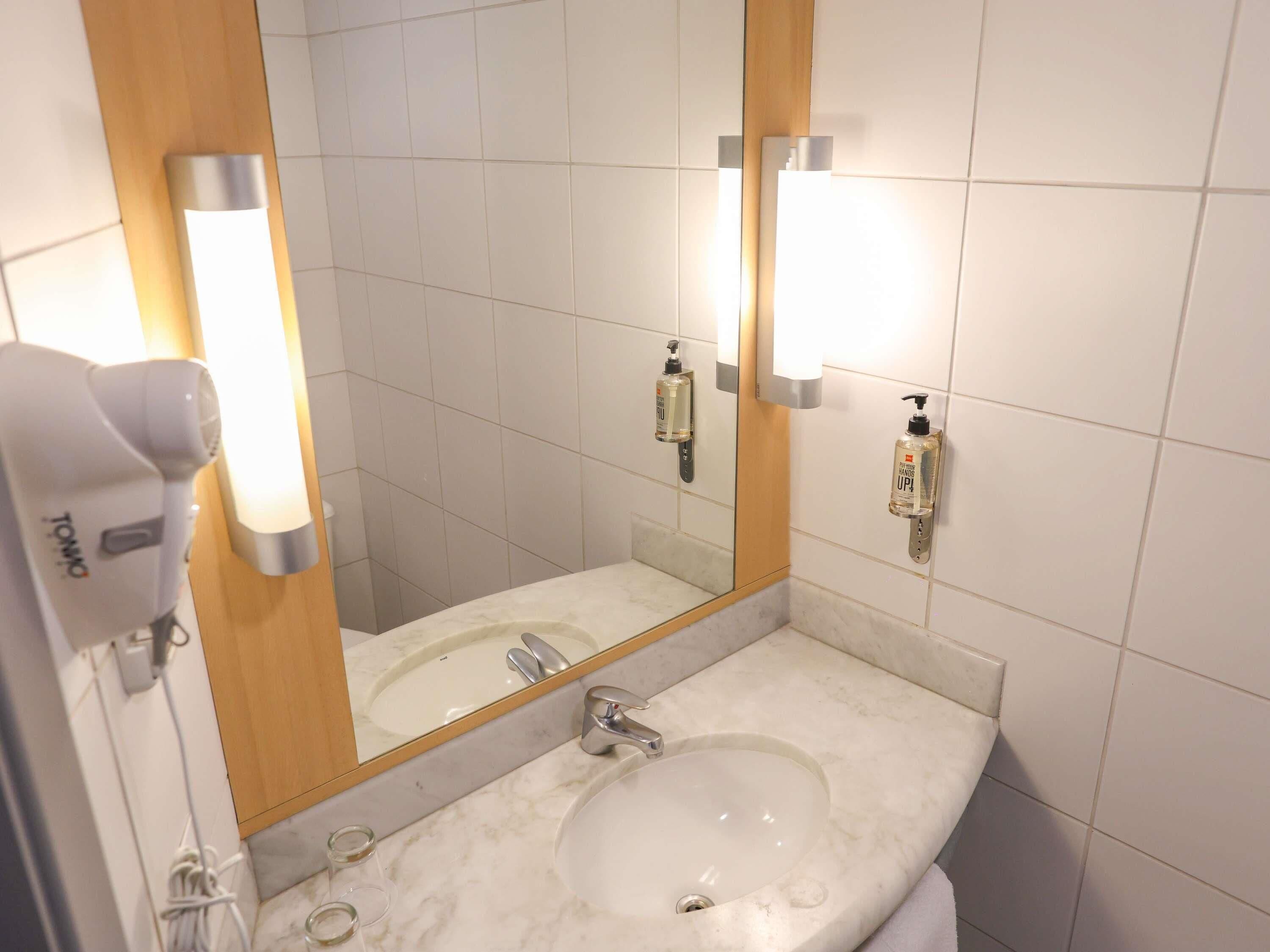 A bathroom with a white sink, a mirror, a hairdryer, and hand sanitizer.