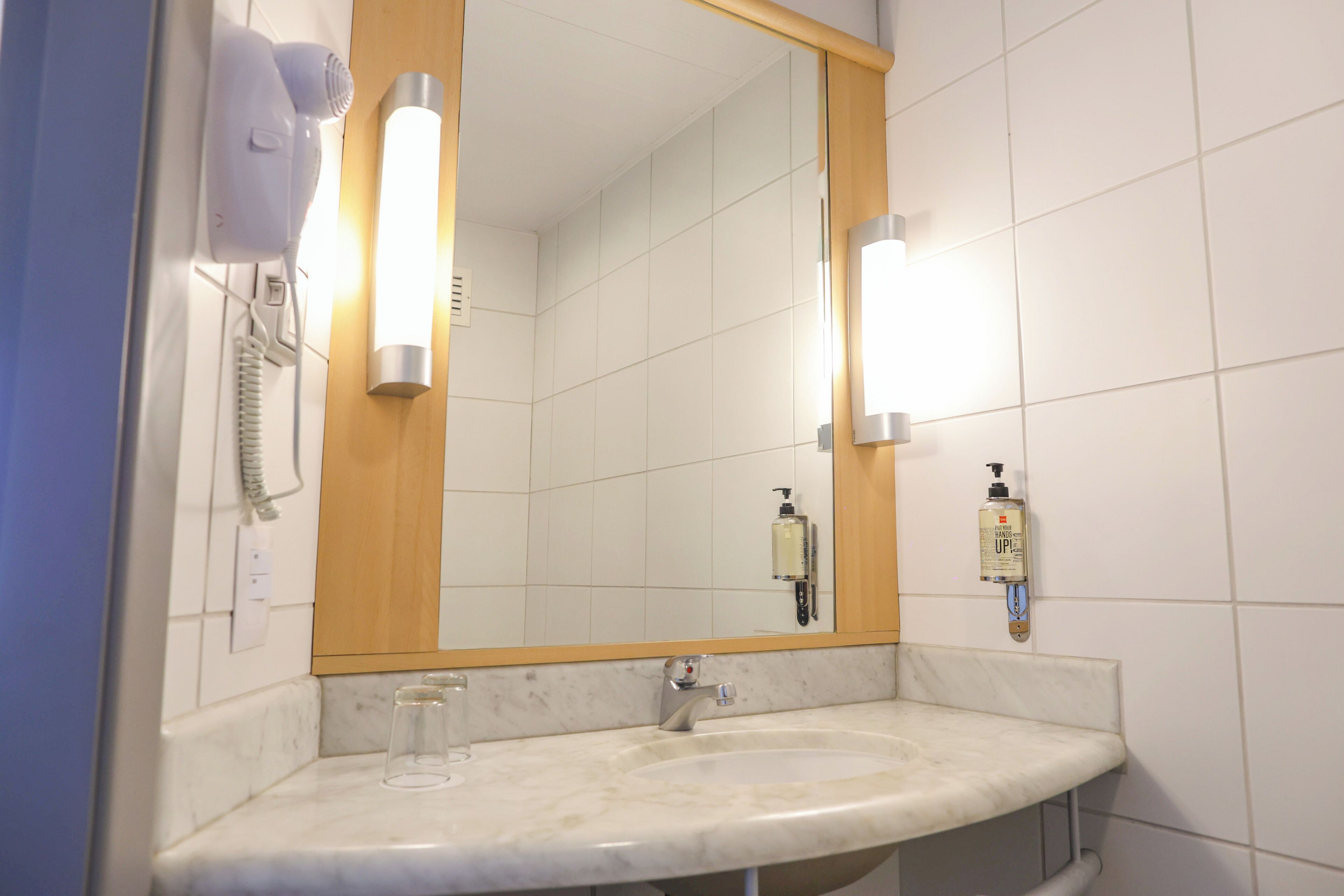 A bathroom with a marble sink, a mirror, a hairdryer, and a hand sanitizer dispenser.