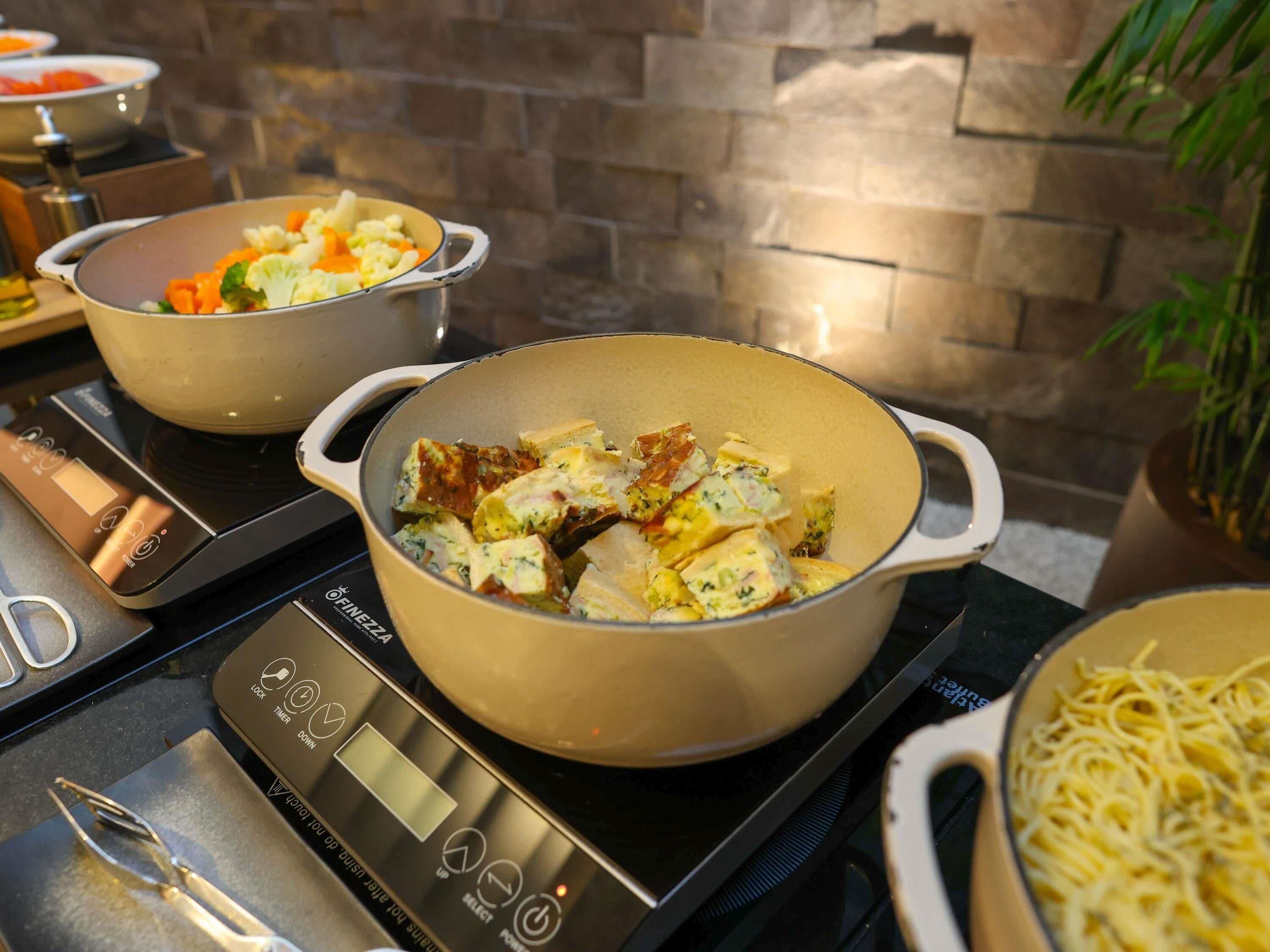 Uma cozinha com uma balança digital, panelas com alimentos e uma parede de tijolos.