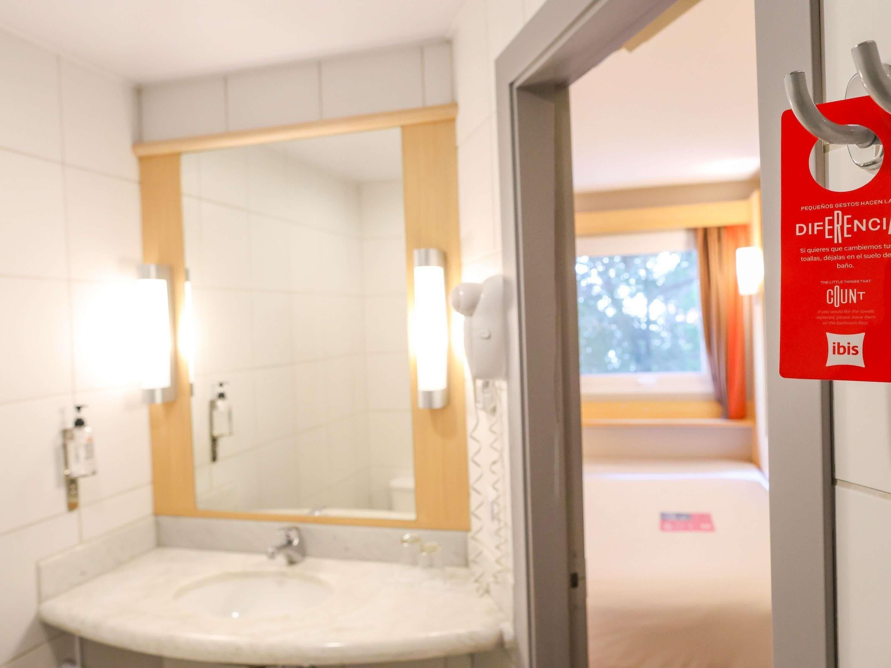 A hotel bathroom with a sink, mirror, and a red sign on the wall.